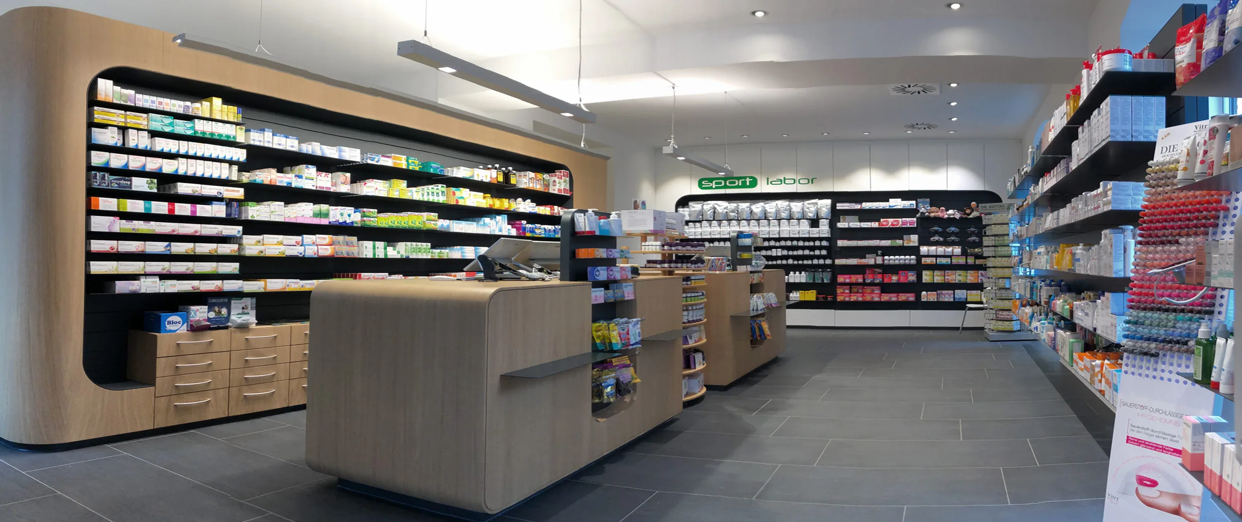 Heller Verkaufsraum der Burggrafen-Apotheke mit Holzverkaufstischen, Regalen voller Arzneimittel und dem sportlabor-Regal im Hintergrund