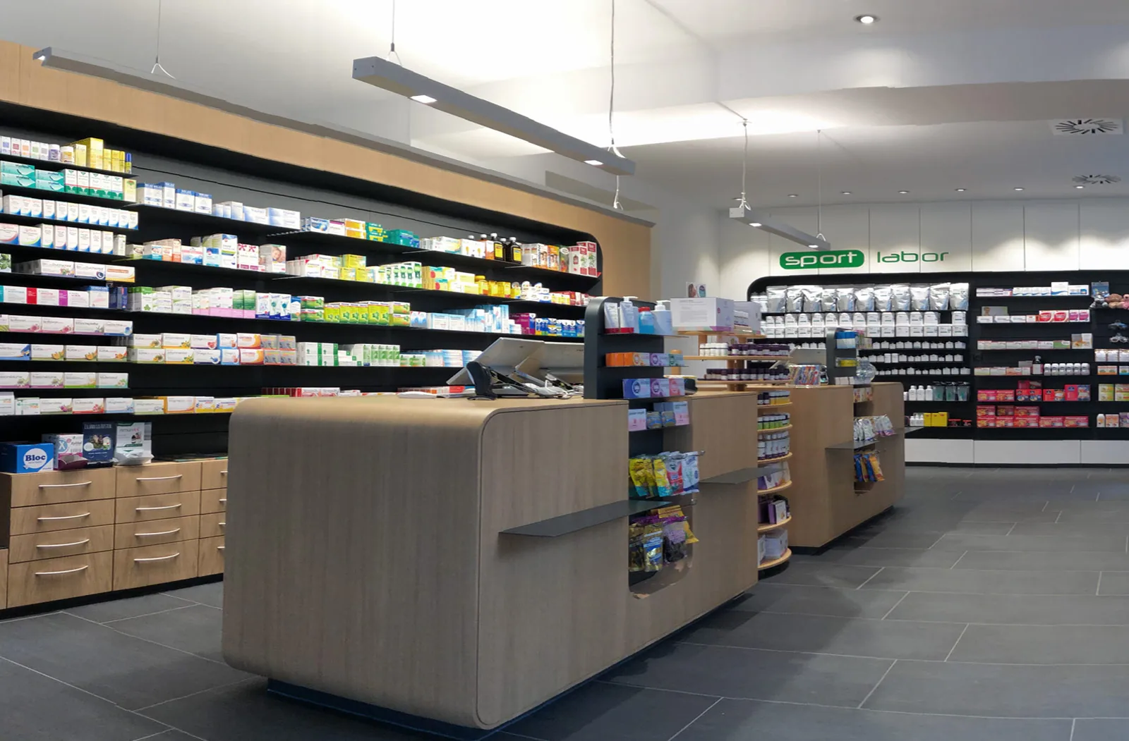 Verkaufsraum der Burggrafen-Apotheke mit geschwungenem Holzregal, Beratungstischen und Freiwahl-Regalen